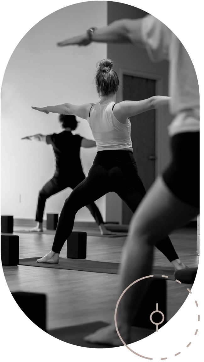A greyscale photograph of yoga students are posed in warrior one, facing away from the camera.